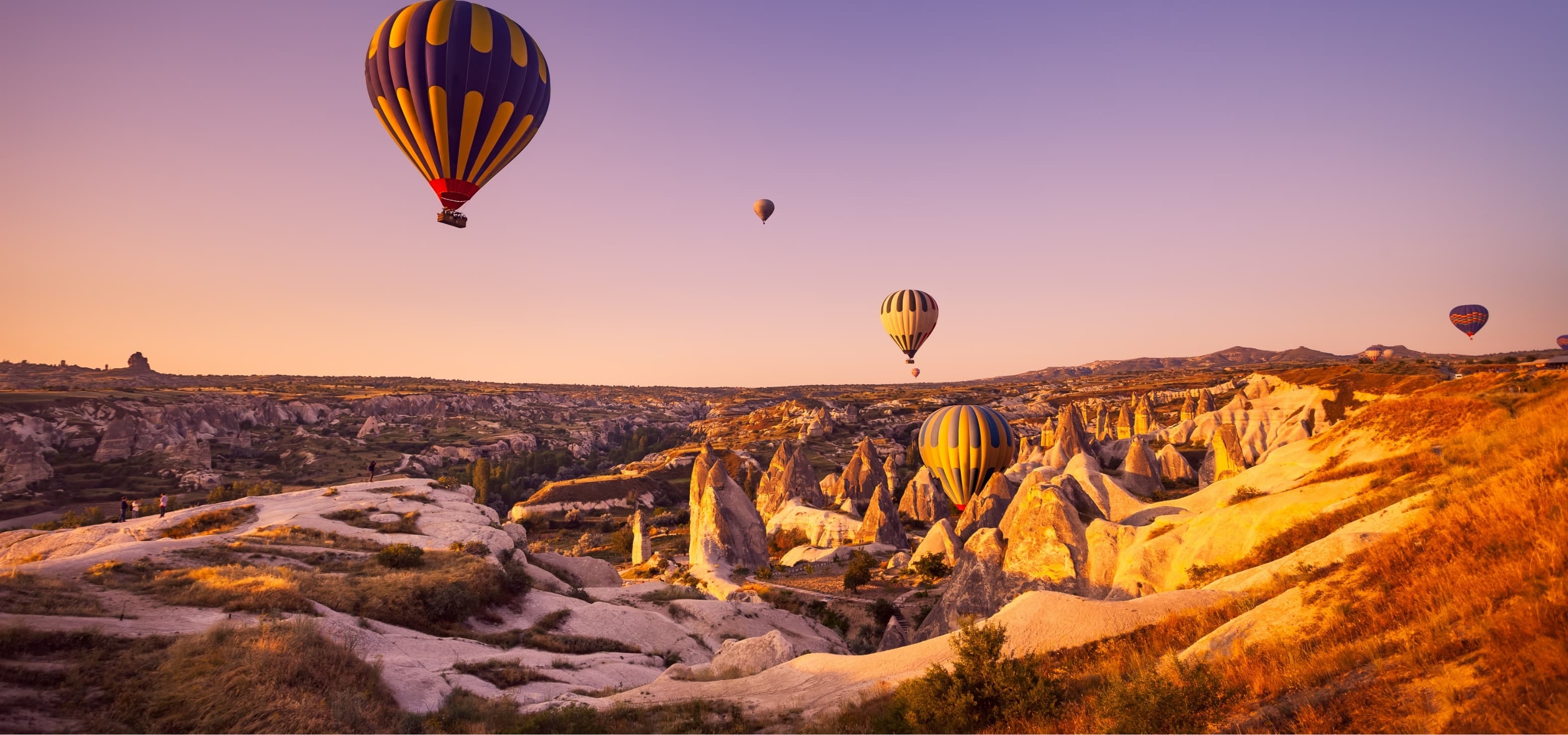 Otel terasından gün doğumunda Kapadokya vadisi üzerinde süzülen sıcak hava balonları